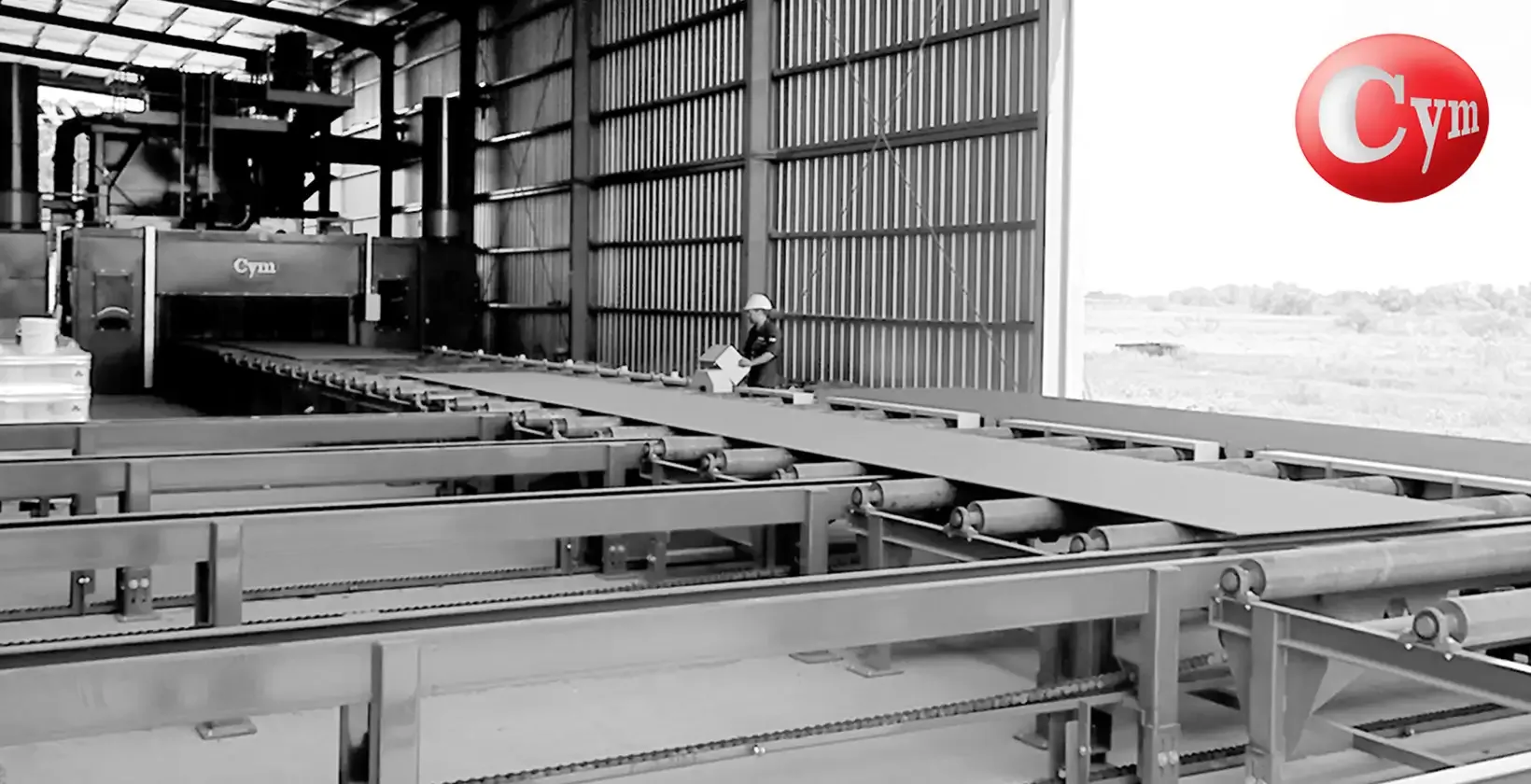 Transfer de salida de granalladora de chapas CYM CH 2.5H – mesa transversal con chapas granalladas sobre rodillos, equipo CYM al fondo, operario supervisando · Astillero Paraná Sur, Argentina