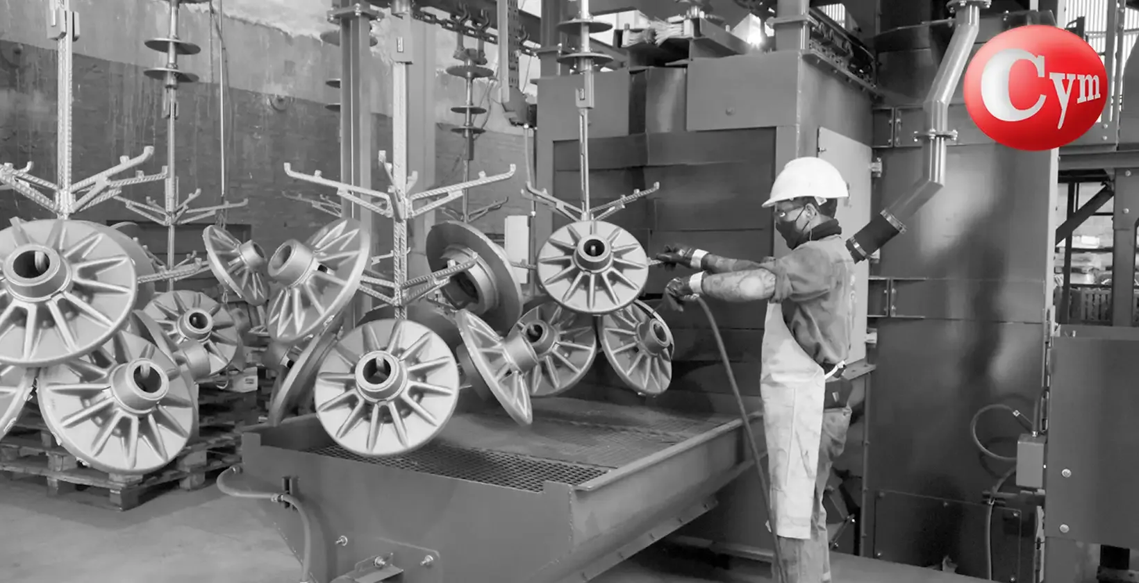 Túnel de granallado de avance continuo CYM TUN 8x10 – operación de carga y descarga de piezas fundidas en transportador aéreo de ganchos